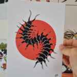 An art print of a centipede, with a red circle behind it. The colour of the centipede is black with white highlights