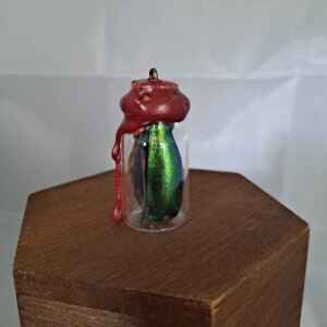 A small, wax sealed glass jar containing green beetle wing cases